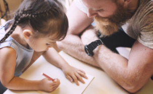 Young girl carefully drawing while her father looks on